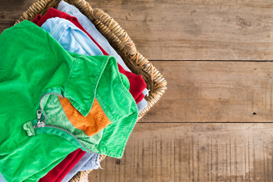 Clean washed unironed summer clothes with a fresh fragrance stacked in a wicker laundry basket with a bright green shirt on top, overhead view on rustic wooden boards with copyspace to the right